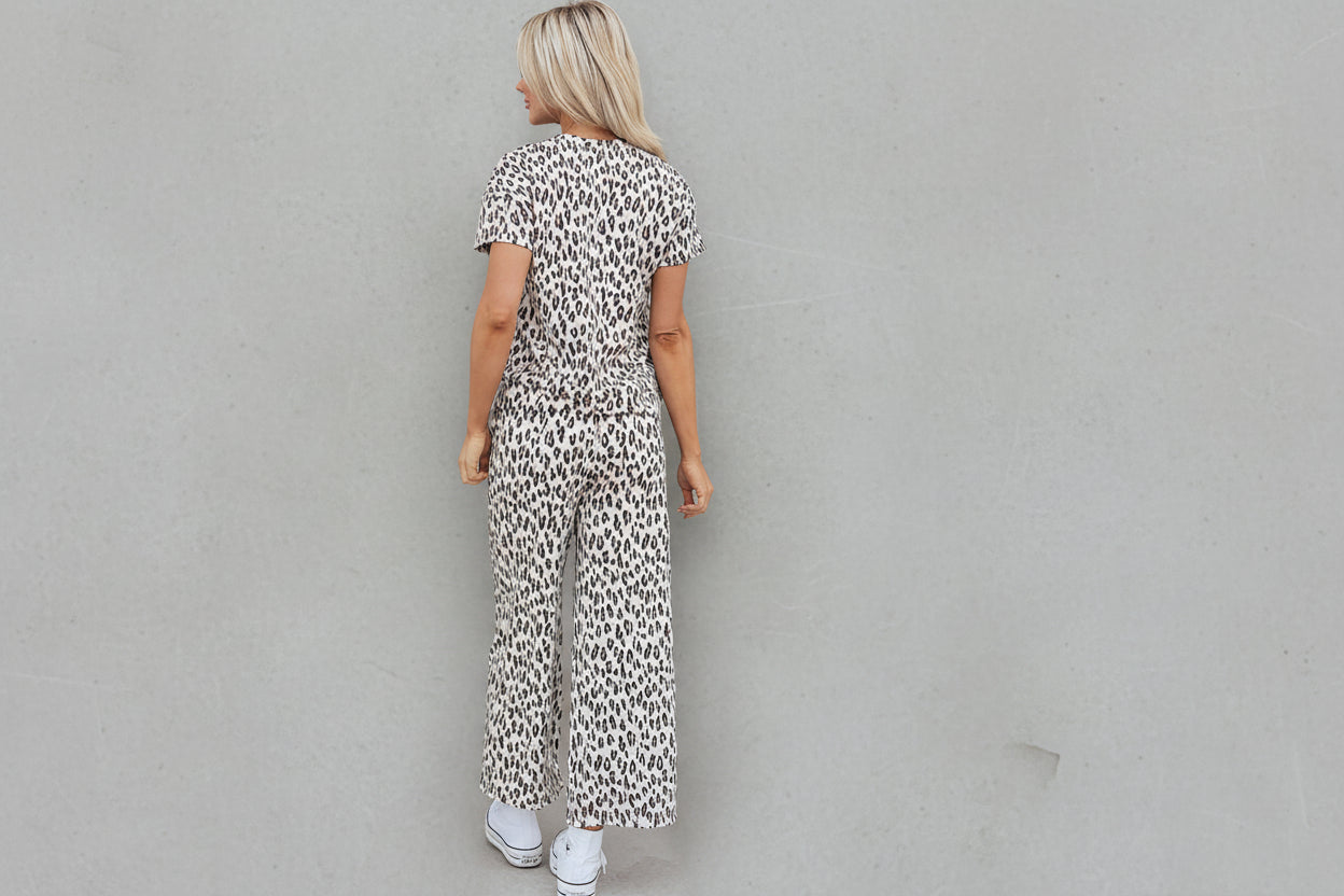 Person wearing a leopard print jumpsuit standing in front of a door with a wreath.